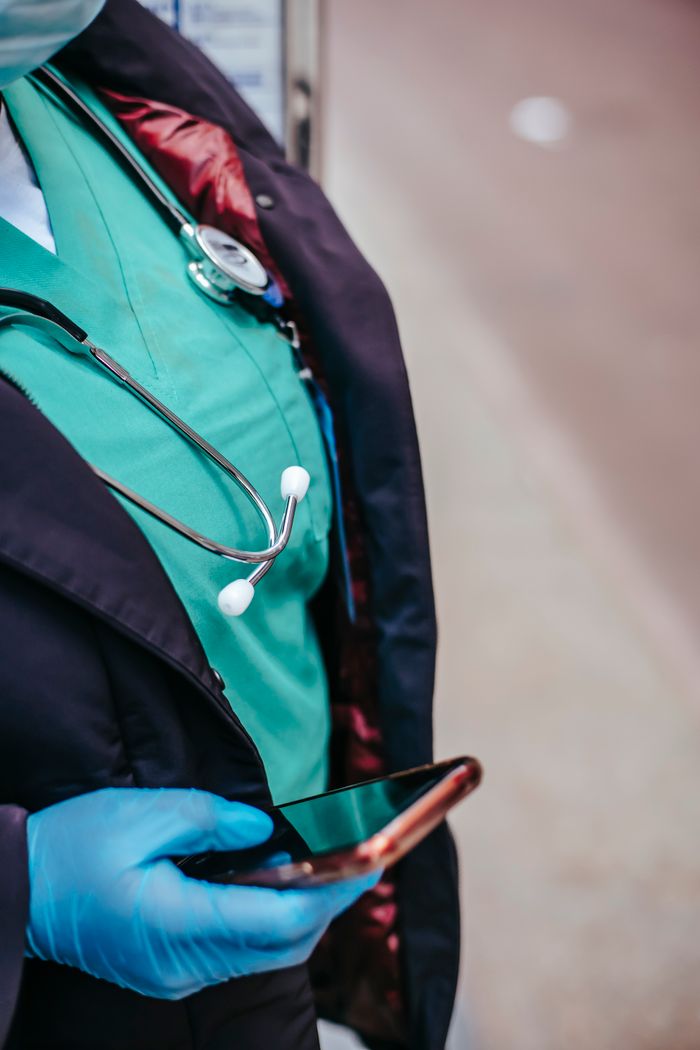 services-02 Crop anonymous female doctor in uniform with stethoscope touching black screen on cellphone in town