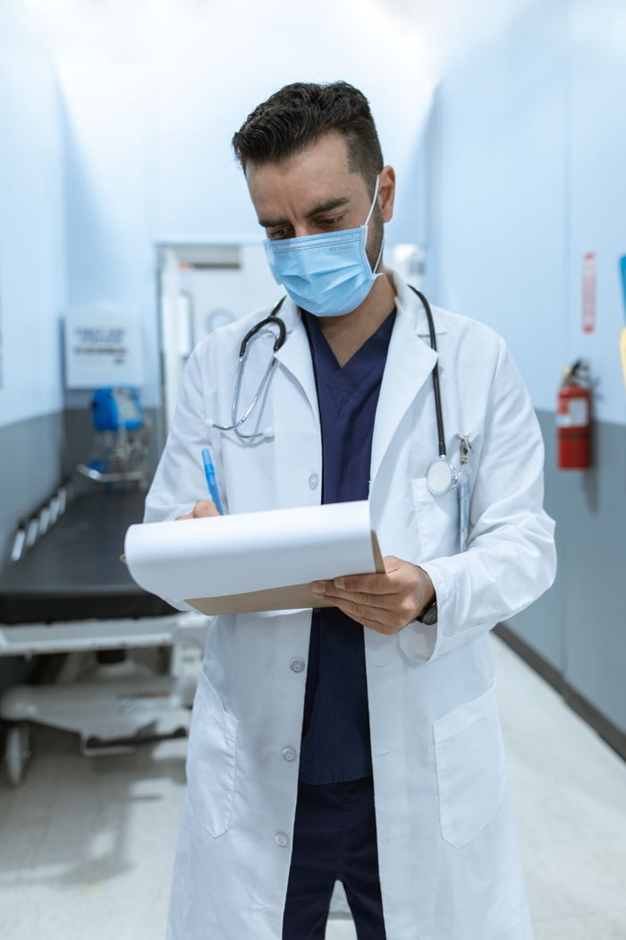 team-01 Medical professional wearing mask, writing on chart in hospital hallway.