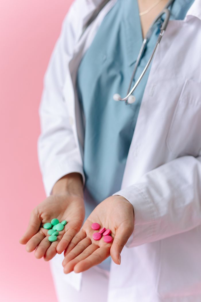 team-05 Medical professional displaying colorful pills in hands on a pink background.